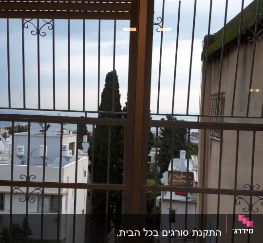 חלון עם סורגים מתכתיים ונוף עירוני ברקע